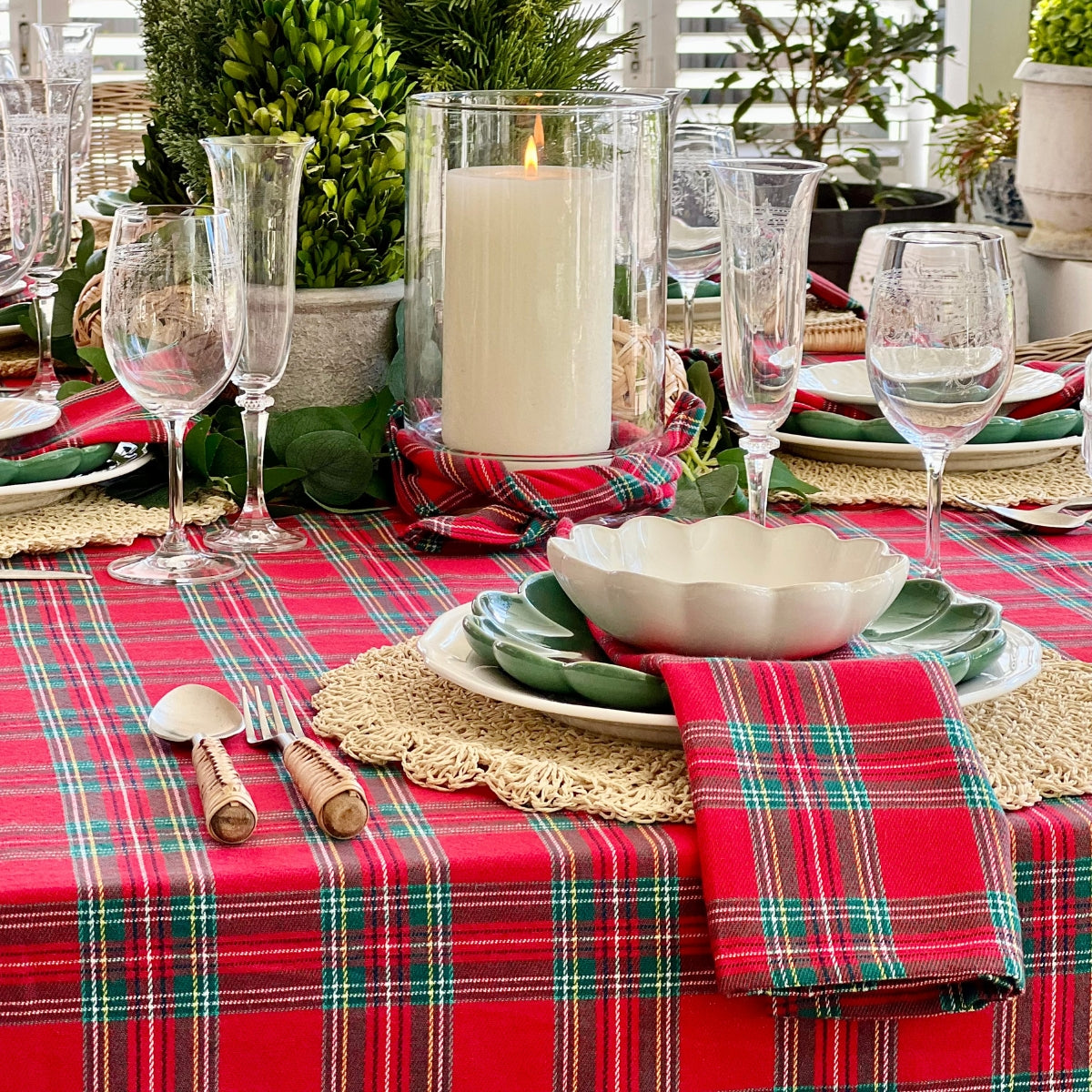 Decorative table setting with red plaid tablecloth, candles, and glasses.