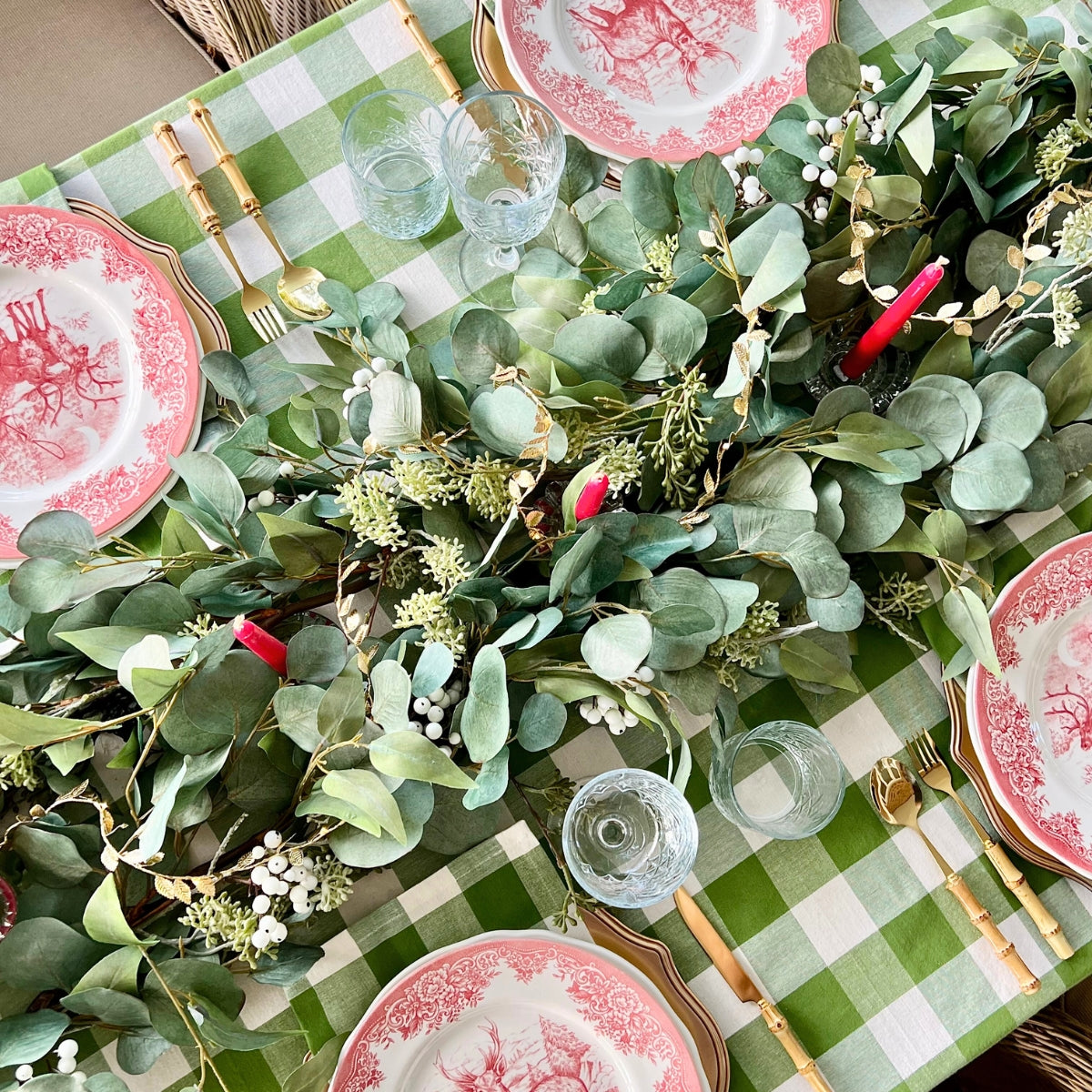 Decorative table setting with greenery, red plates, and gold cutlery on a checkered tablecloth.