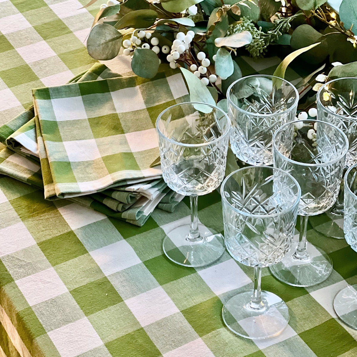 Set of crystal glasses on a green checkered tablecloth with decorative elements.