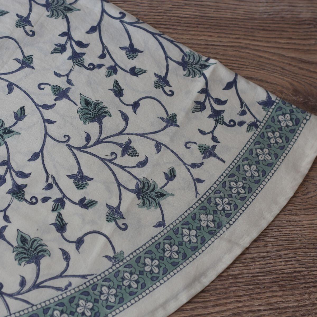 Close up of a circular dining tablecloth featuring a blue and green floral hand block printed pattern
