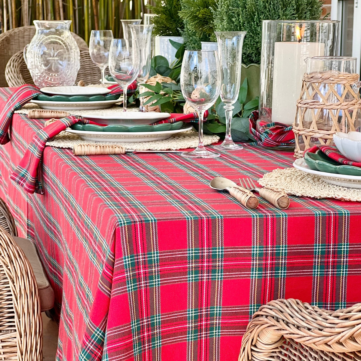 Handwoven red plaid square tablecloth from Decor Mantra’s exclusive holiday collection styled here on a large table woth votives, glasses, candles, dishes and foilage in holiday setting.