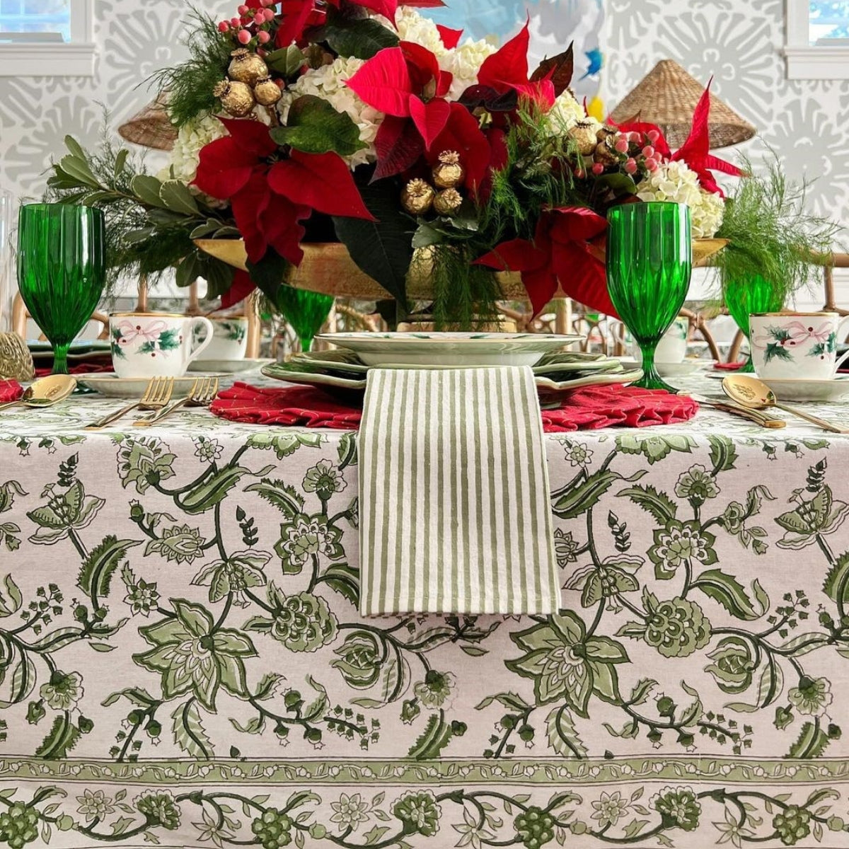Decorative Christmas table setting with floral centerpieces, green glasses, and patterned tablecloth.