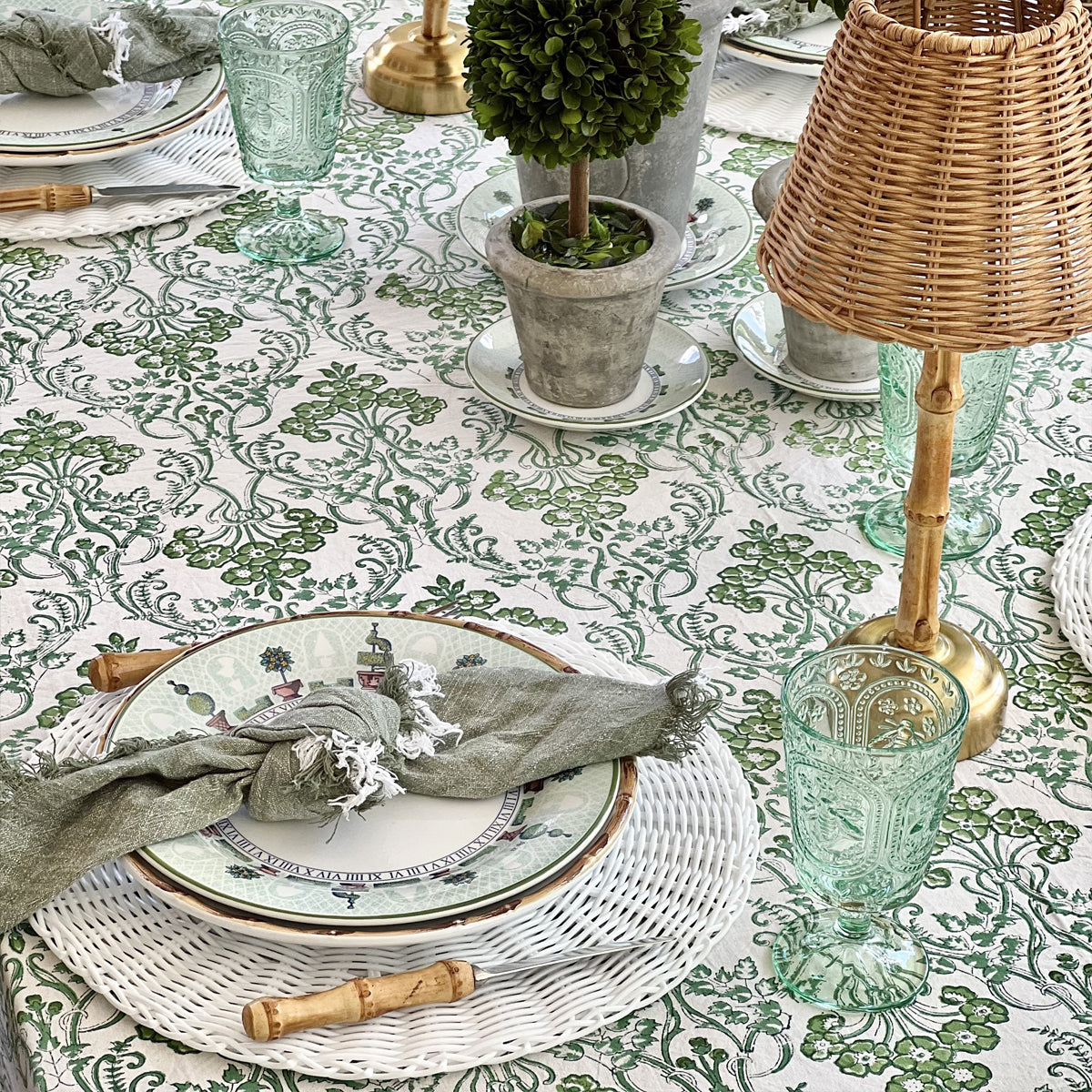 Detail of a green floral hand block printed tablecloth in 180 x 270 cm with patterned plates, bamboo handled cutlery and green glasses for eight to ten guests