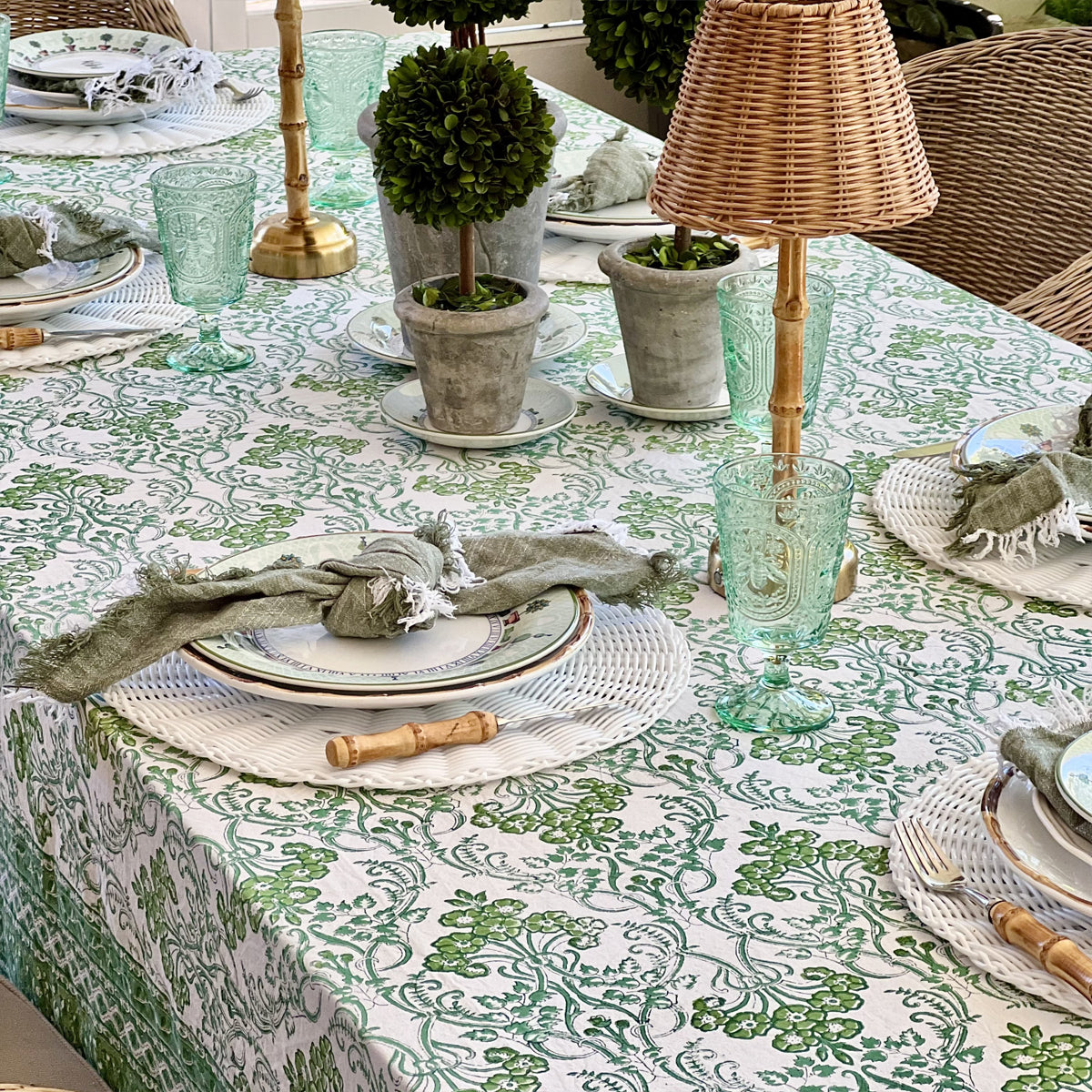 Green floral hand block printed tablecloth in 152 x 225 cm set for a six seater lunch with topiary, a rattan lamp and sage linen napkins