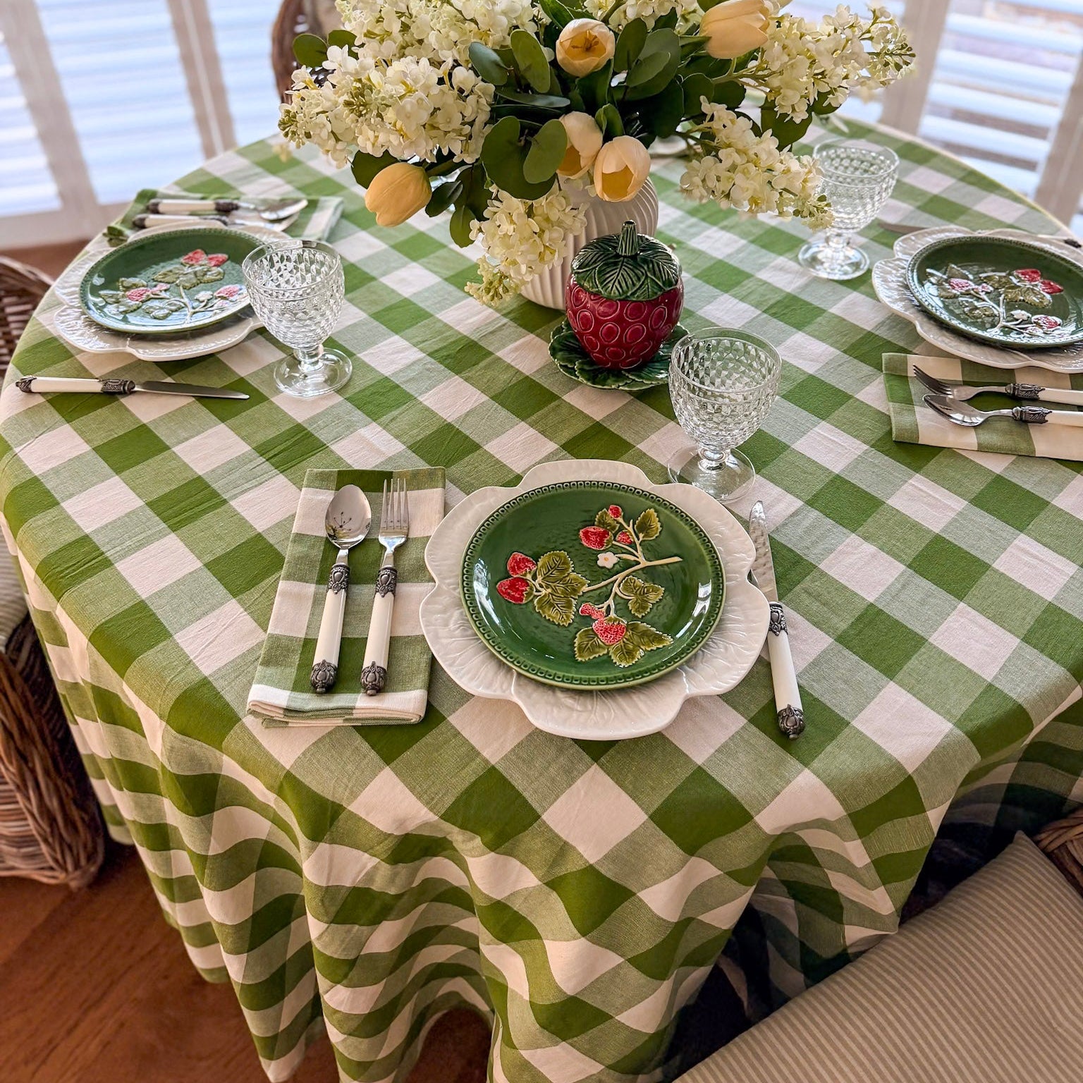 Dining table set with a green and white checkered tablecloth, floral centerpiece, and decorative plates.