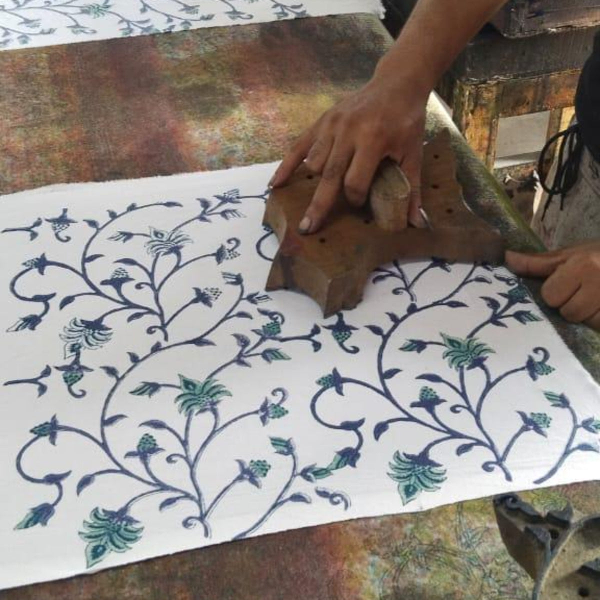 Artisan block printing a floral pattern in blue and green on premium cotton for round table linens.