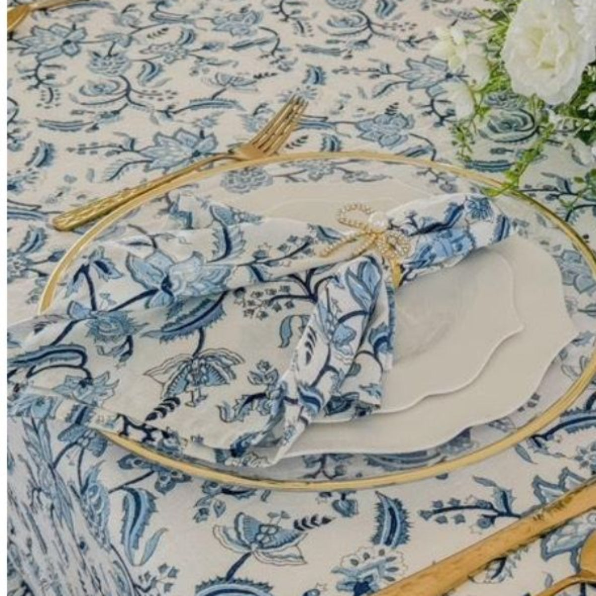 A set of four blue and white hand block printed chintz floral patterned napkins on a table with cutlery and a white tablecloth.