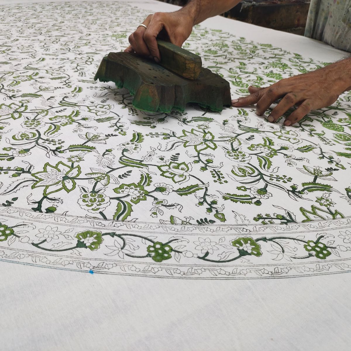 A skilled artisan hand pressing a carved wooden block onto premium cotton fabric, printing the Chintz monochrome green intricate floral pattern in a small batch Indian block printing process.