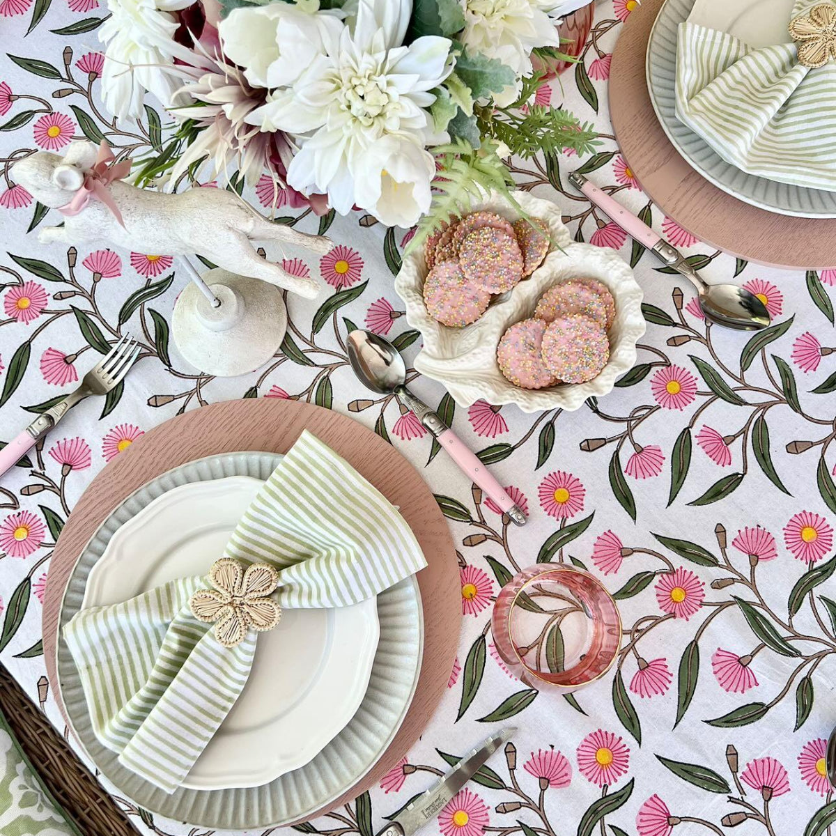 Pink Green Flowering Gums tablecloth styled for an 8 to 10-seater Easter celebration with cookies, donuts, bunny décor, fresh flowers, and green striped napkins.