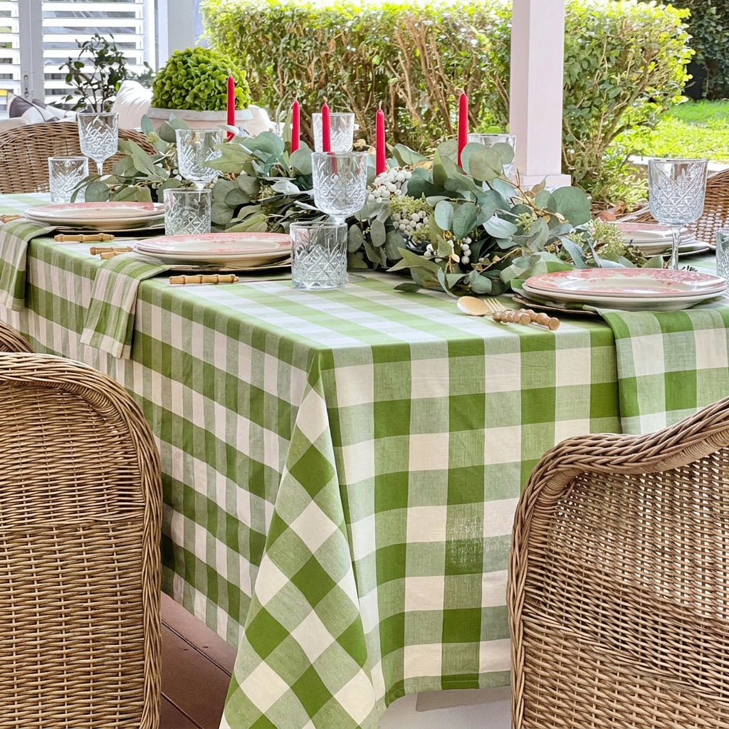A large green gingham check woven table linen on a 10 to 12 seater holiday dining table, featuring red decorative plates, red candles, eucalyptus and green foliage centrepiece, and green gingham napkins folded neatly beneath each plate, ideal for festive Australian Christmas entertaining.