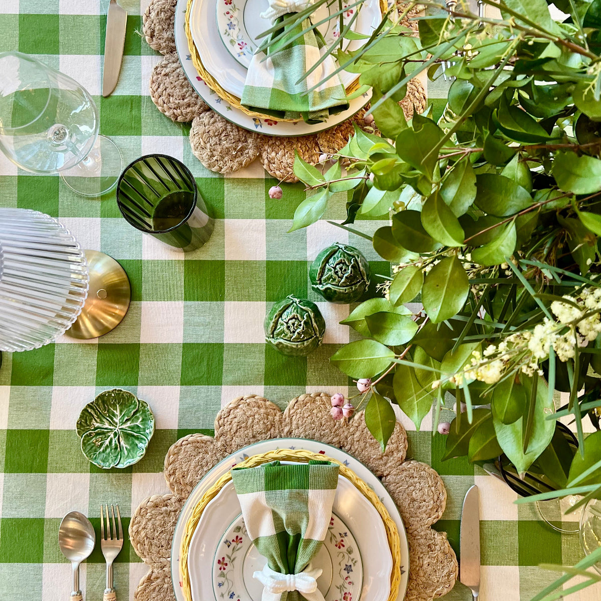 Top-down view of an elegant table setting with green checkered tablecloth, decorative plates, and floral centerpieces.