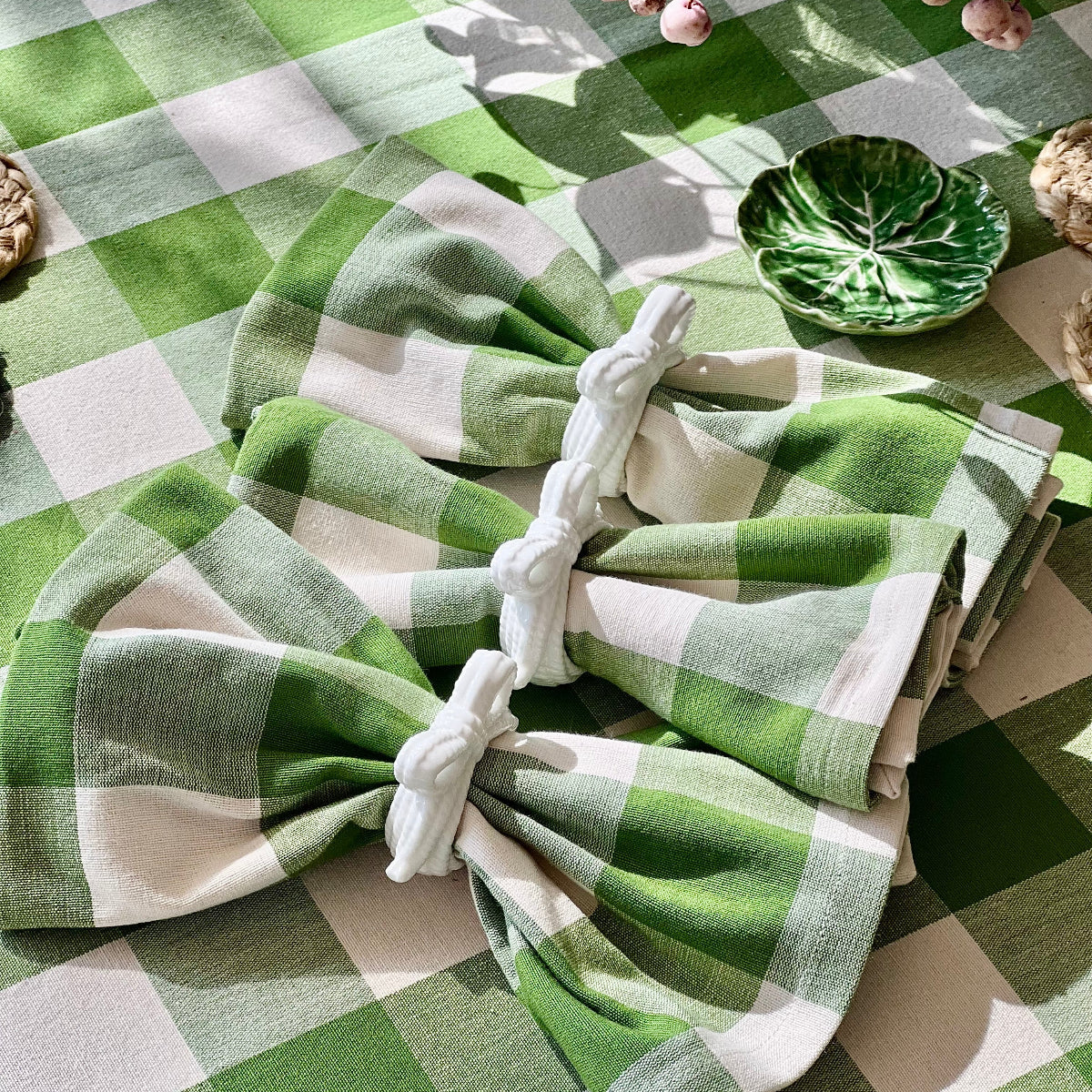 Close up view of a 225 cm round green gingham check handwoven cotton tablecloth on a large circular dining table, with Green and white checkered folded napkins in white napkin rings