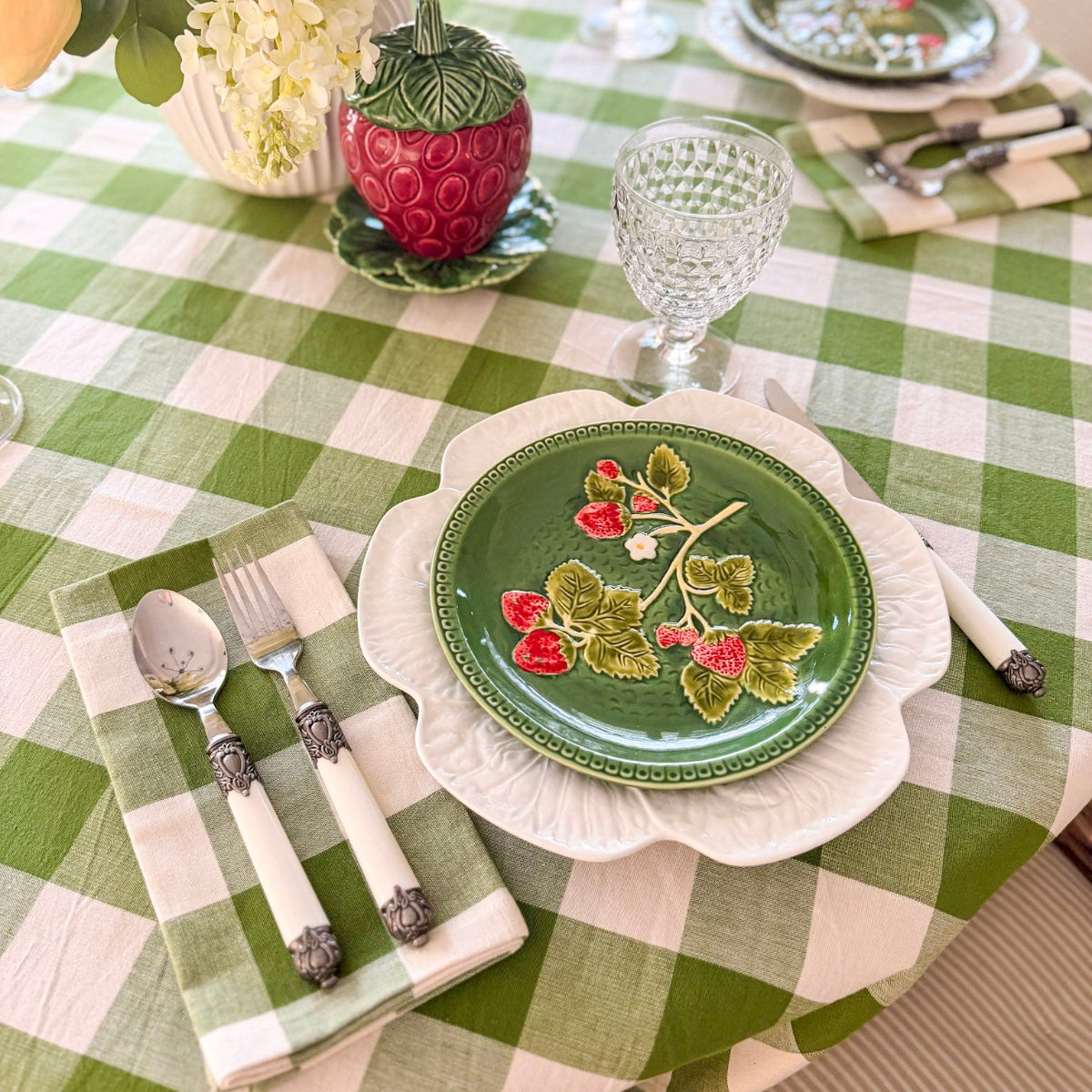 A cosy round dining table set on a green gingham check handwoven tablecloth for a charming effortless table for everyday meals.