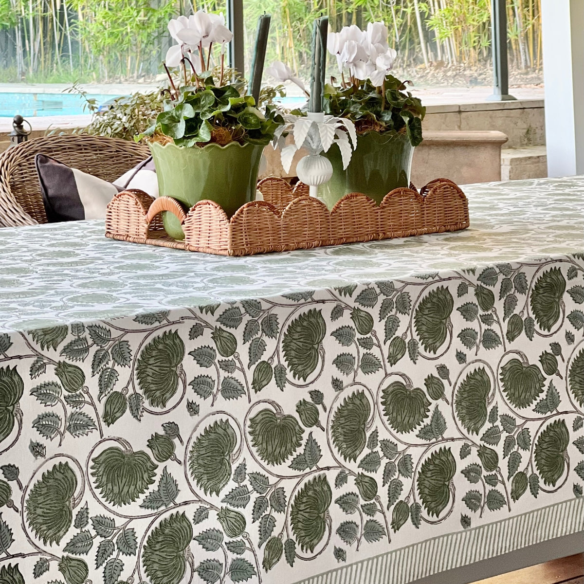 A 180 x 270 cm green lotus hand block printed cotton tablecloth on a large dining table with a wicker basket plant, an 8 to 10 seater table linen in rich green floral block print on premium cotton.