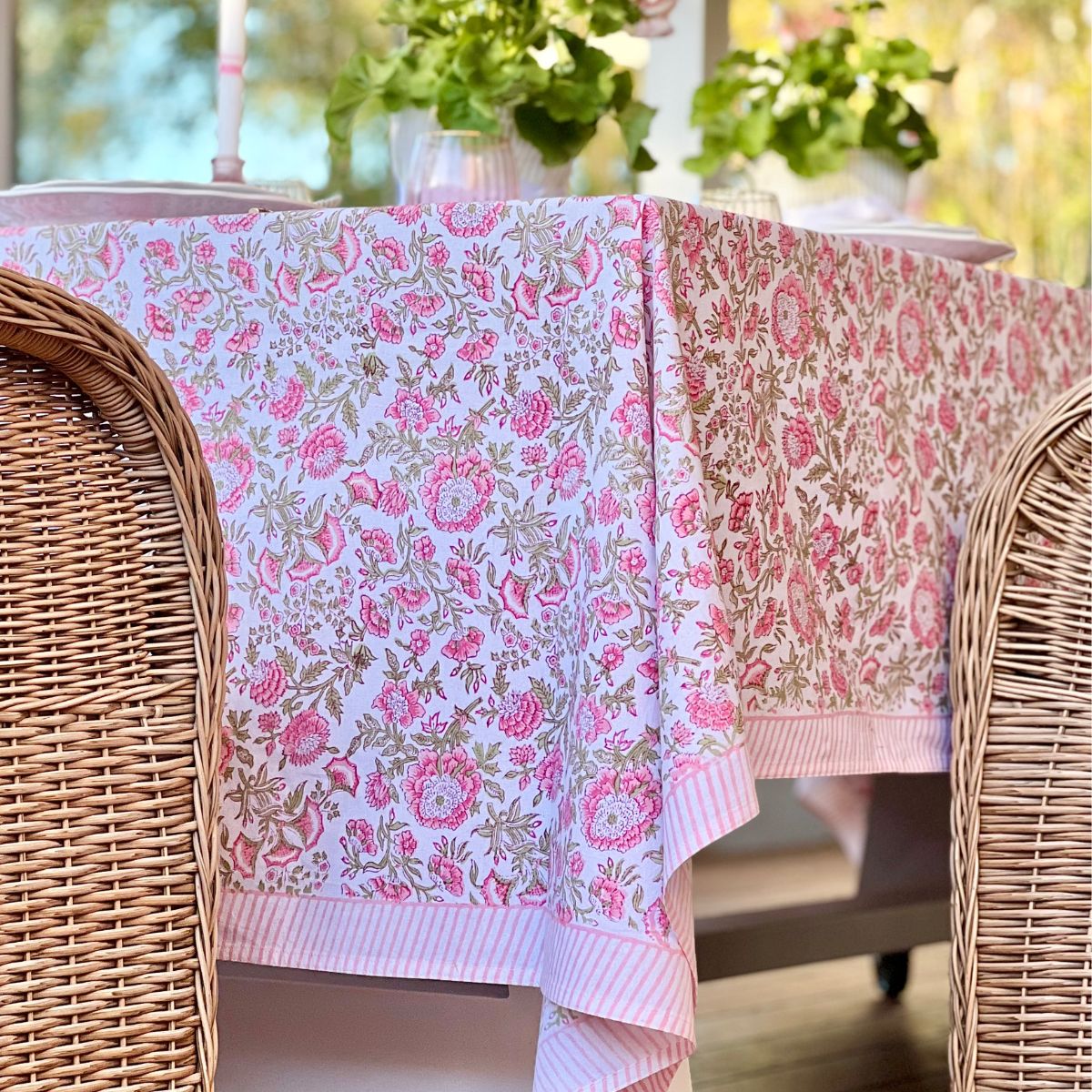 Side view of hand-crafted rectangular tablecloth with a Beatrice floral motif in pink and green tones, set on an outdoor dining table with wooden chairs.