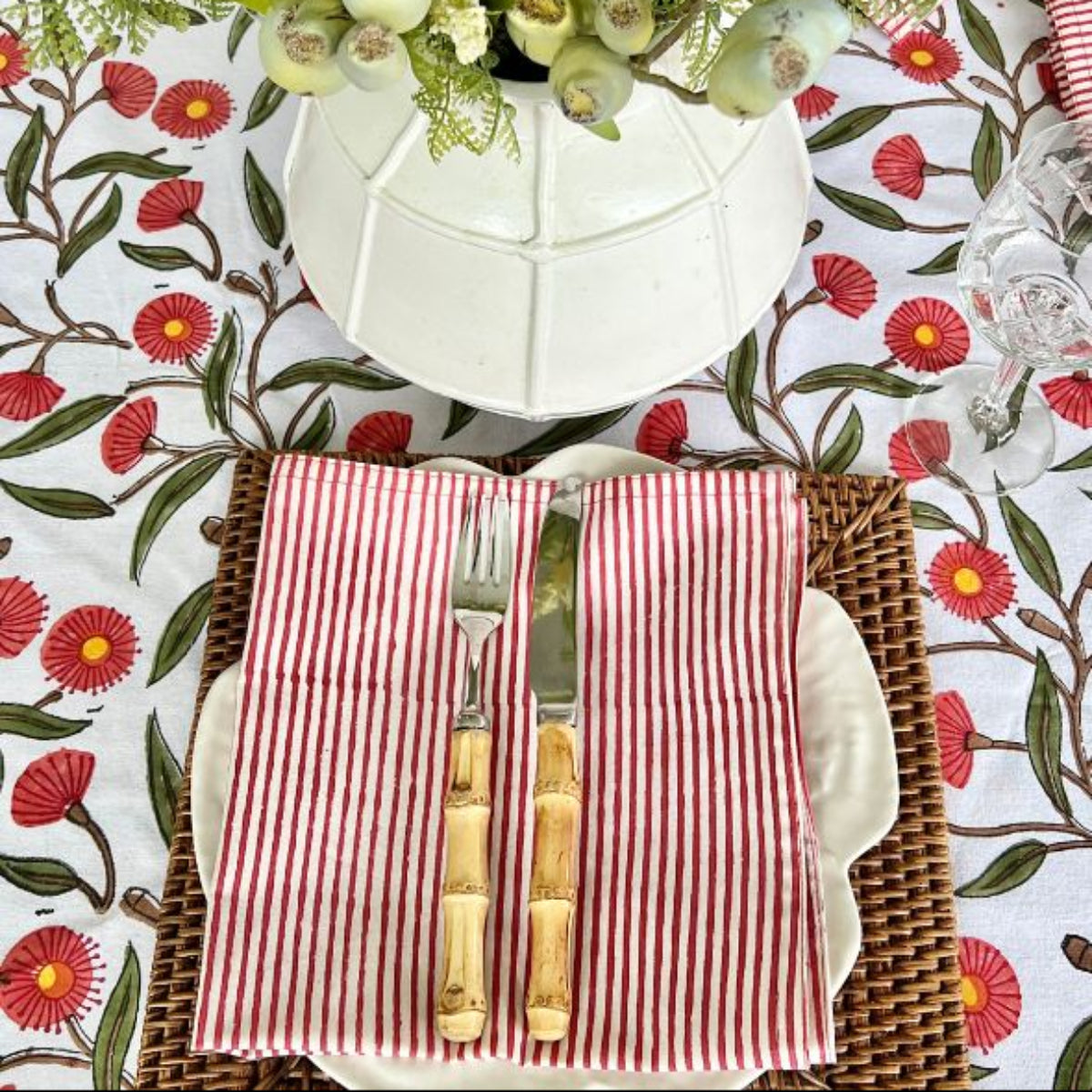 A red striped hand block printed cotton napkin on a casual everyday dining table, styled with a floral vase and bamboo cutlery for a relaxed informal place setting.