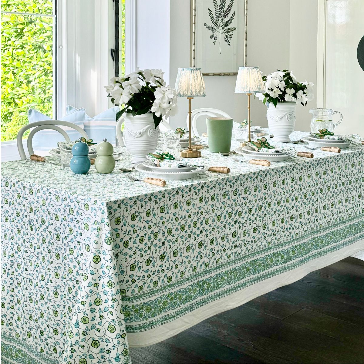 A rectangular floral hand block printed pattern tablecloth hand block printed in shades of green and blue, displayed on a table with dishes and decorative items.