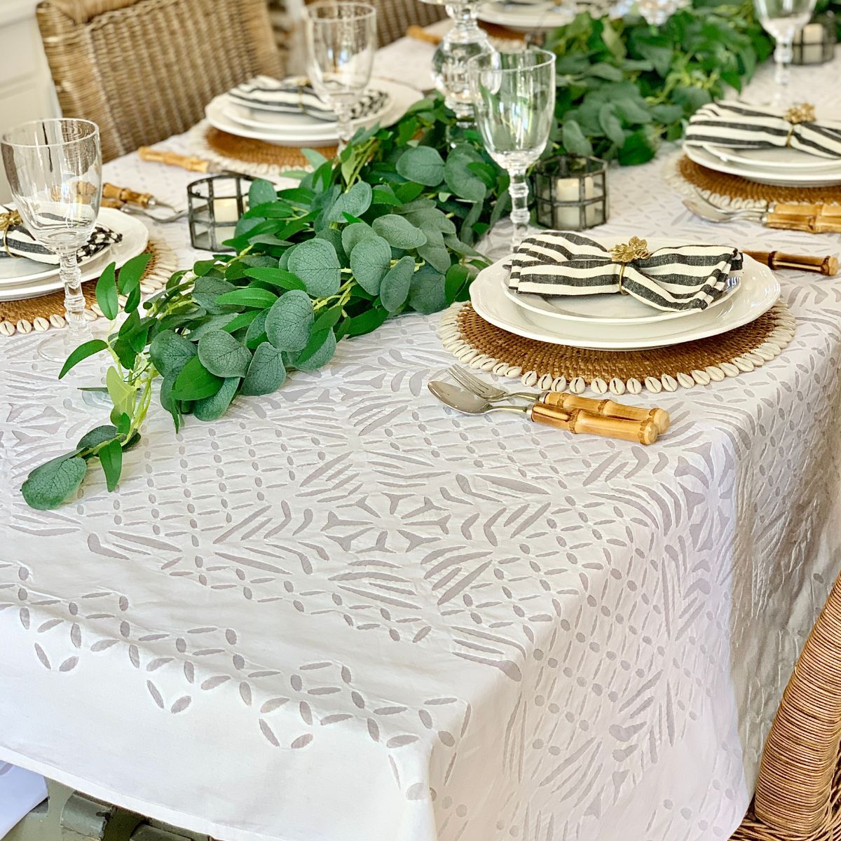 A white rectangular tablecloth with geometric applique cutwork, displayed on a table set with dishes and silverware.