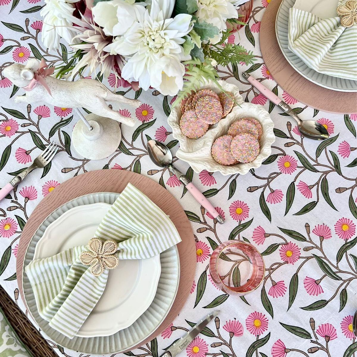 Green striped cotton napkins folded over dinner plates on a pink and green floral tablecloth, creating a fresh tablescape for everyday dining and special occasions.
