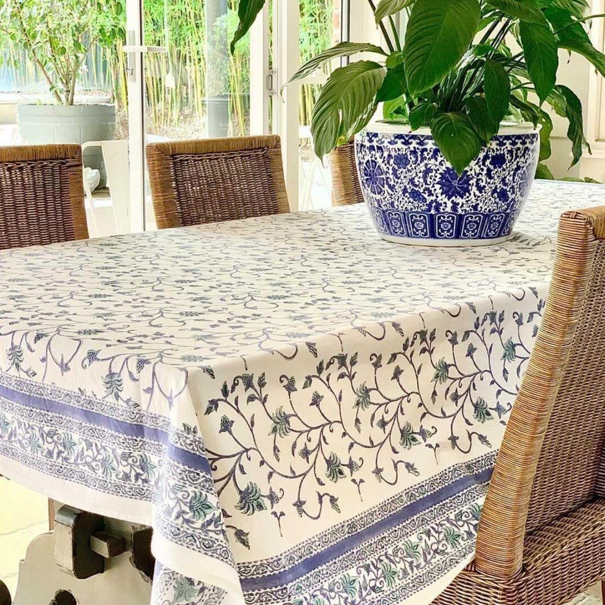 Hand block printed blue and green floral pattern on rectangular tablecloth with wicker chairs in alfresco setting