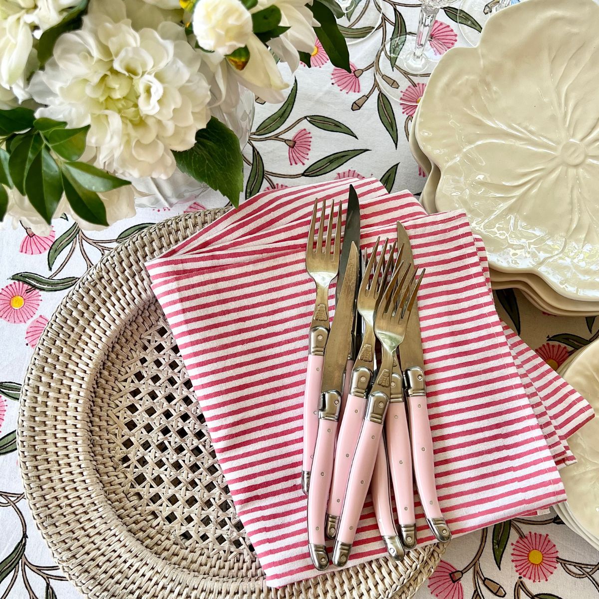 Hand block printed pink striped serviettes crafted from cotton, styled on a floral tablecloth and suitable for everyday meals and special occasions.