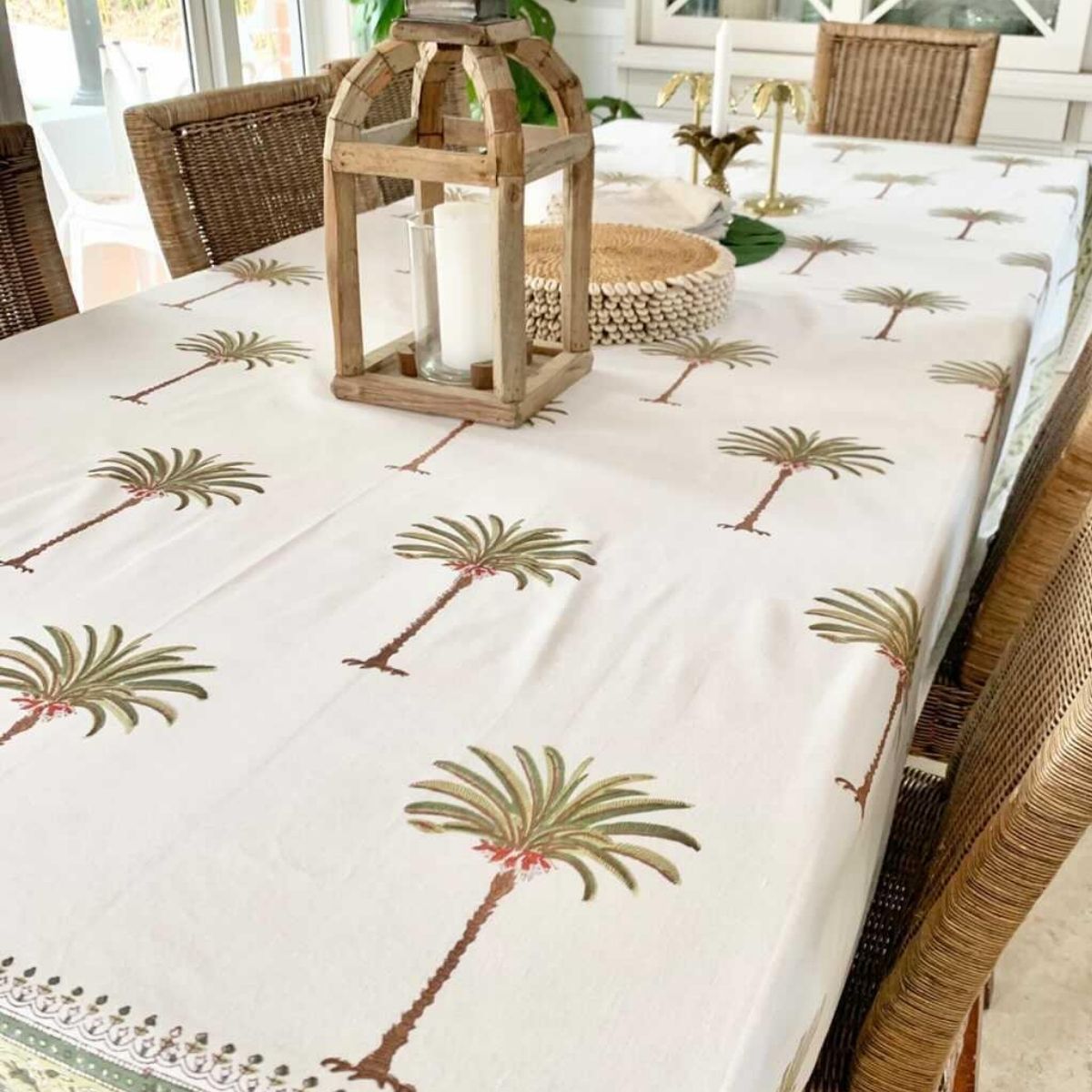 A hand block printed tablecloth with green palm coastal motifs on a white cotton base, displayed on a rectangular table with plates, cutlery, and a floral centerpiece.