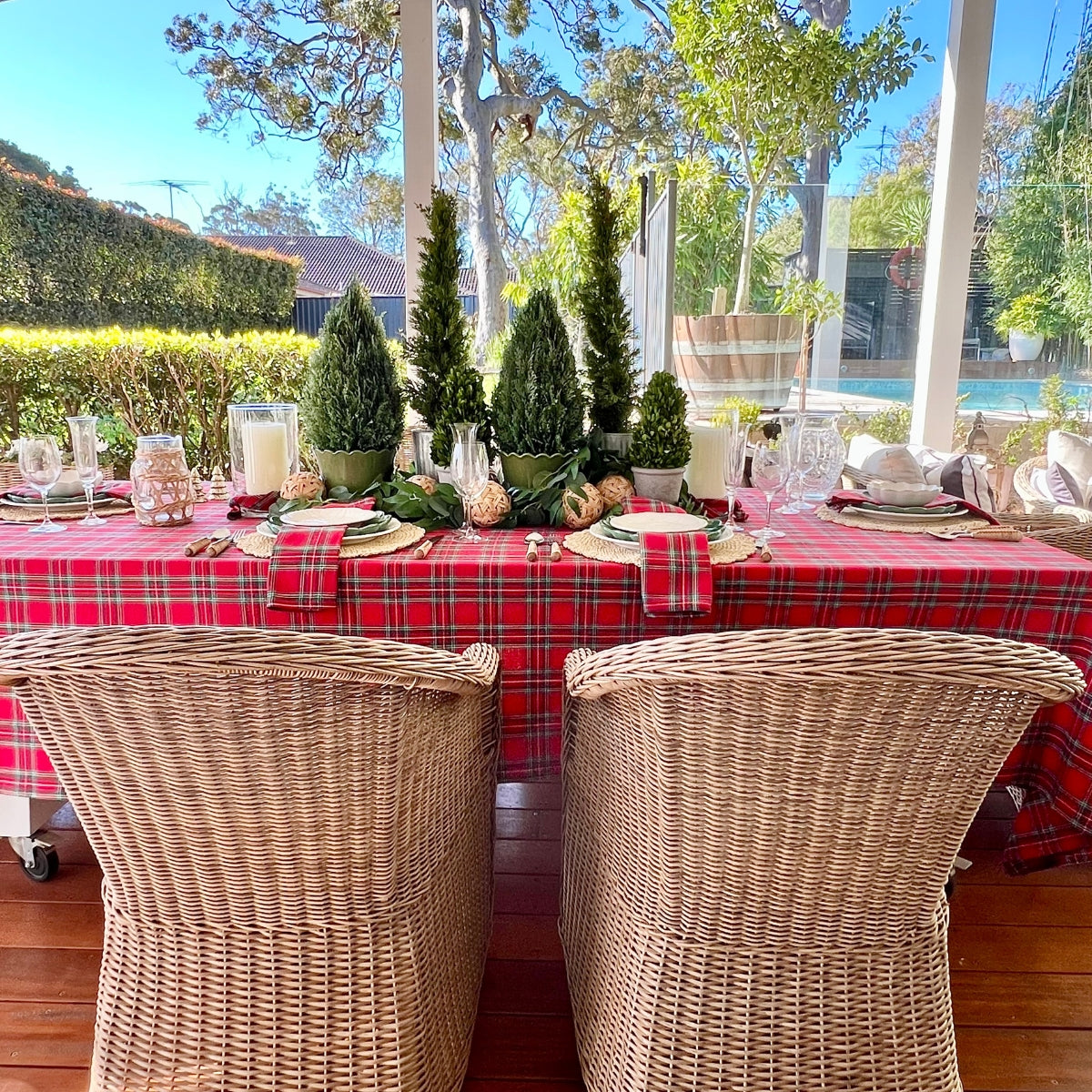 Dining table set with a red plaid tablecloth, candles, and decorative items outdoors.
