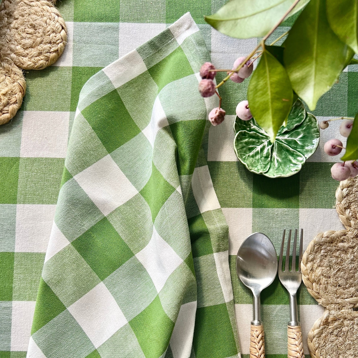 Green and white checkered tablecloth with silverware, plates, and decorative elements on a checkered tablecloth background.
