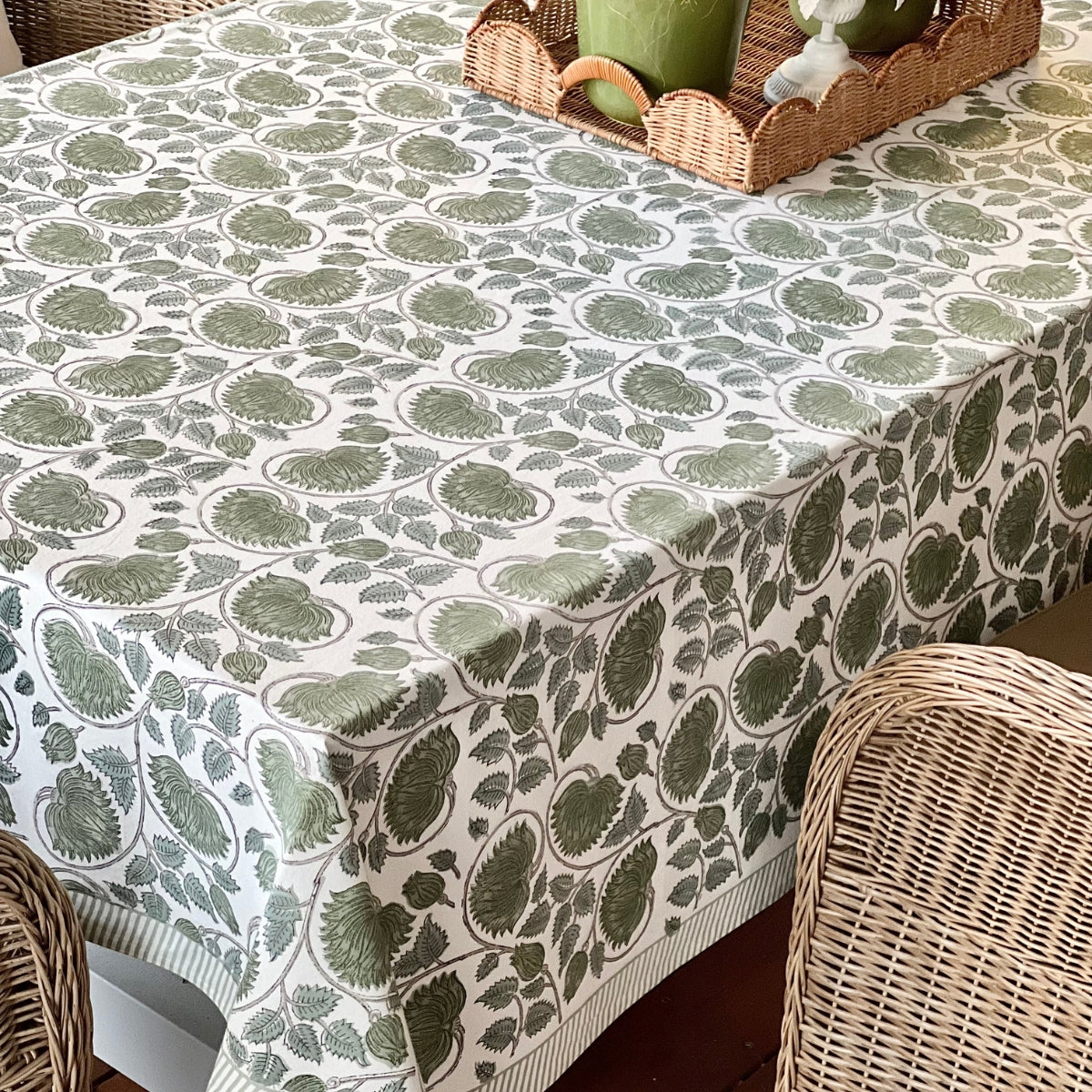 A hand block printed green lotus tablecloth on a table with a wicker chair and a decorative basket in the background.