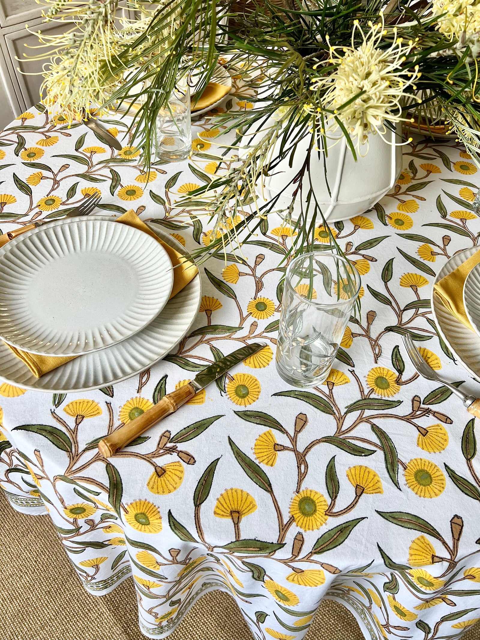 A yellow green round tablecloth with a floral hand block printed pattern featuring gum trees floral pattern, displayed on a table.