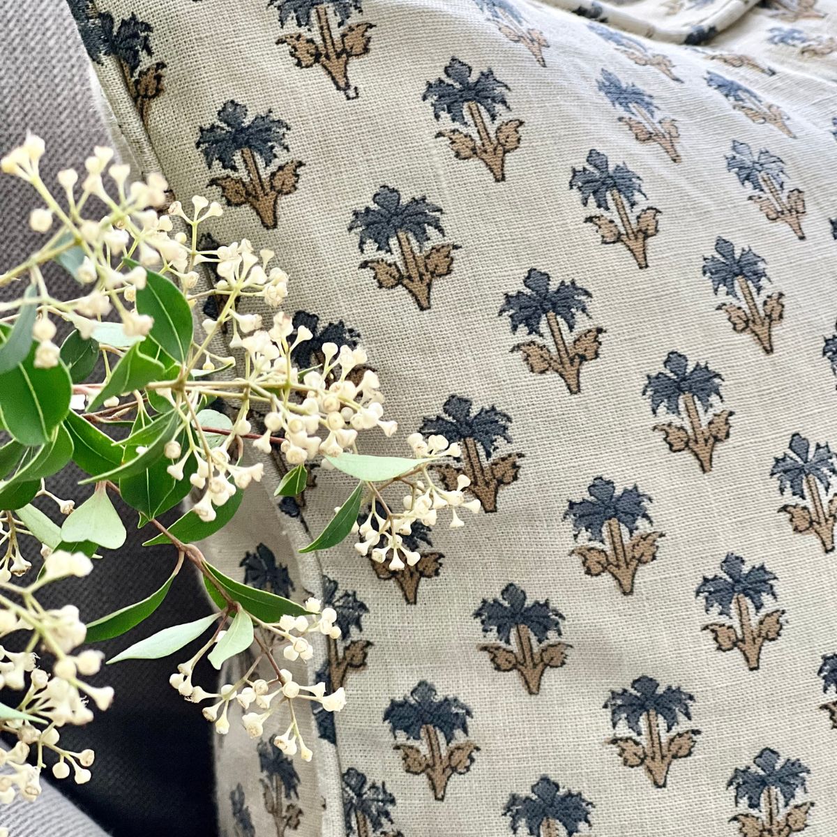 A 50 x 50 cm blue palm booti hand block printed linen cushion cover, angled shot on a sofa showing the small blue sage green floral booti motif across the pure linen fabric.