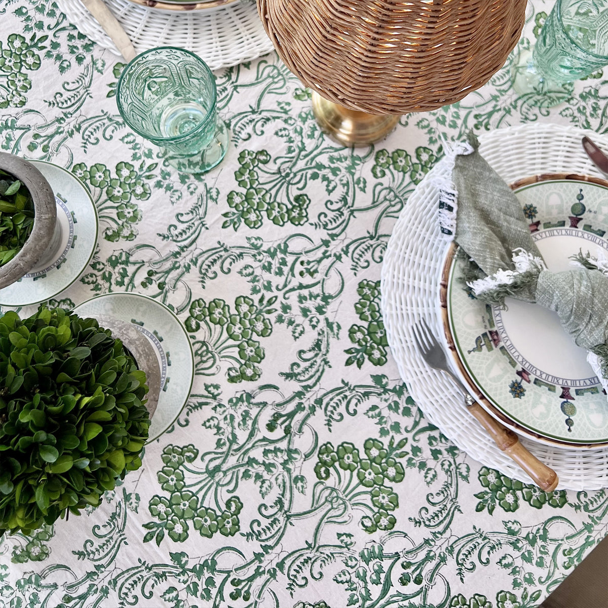 Close up of a green and white floral motif hand block printed tablecloth set for a special gathering with a white woven placemat and bamboo handled cutlery