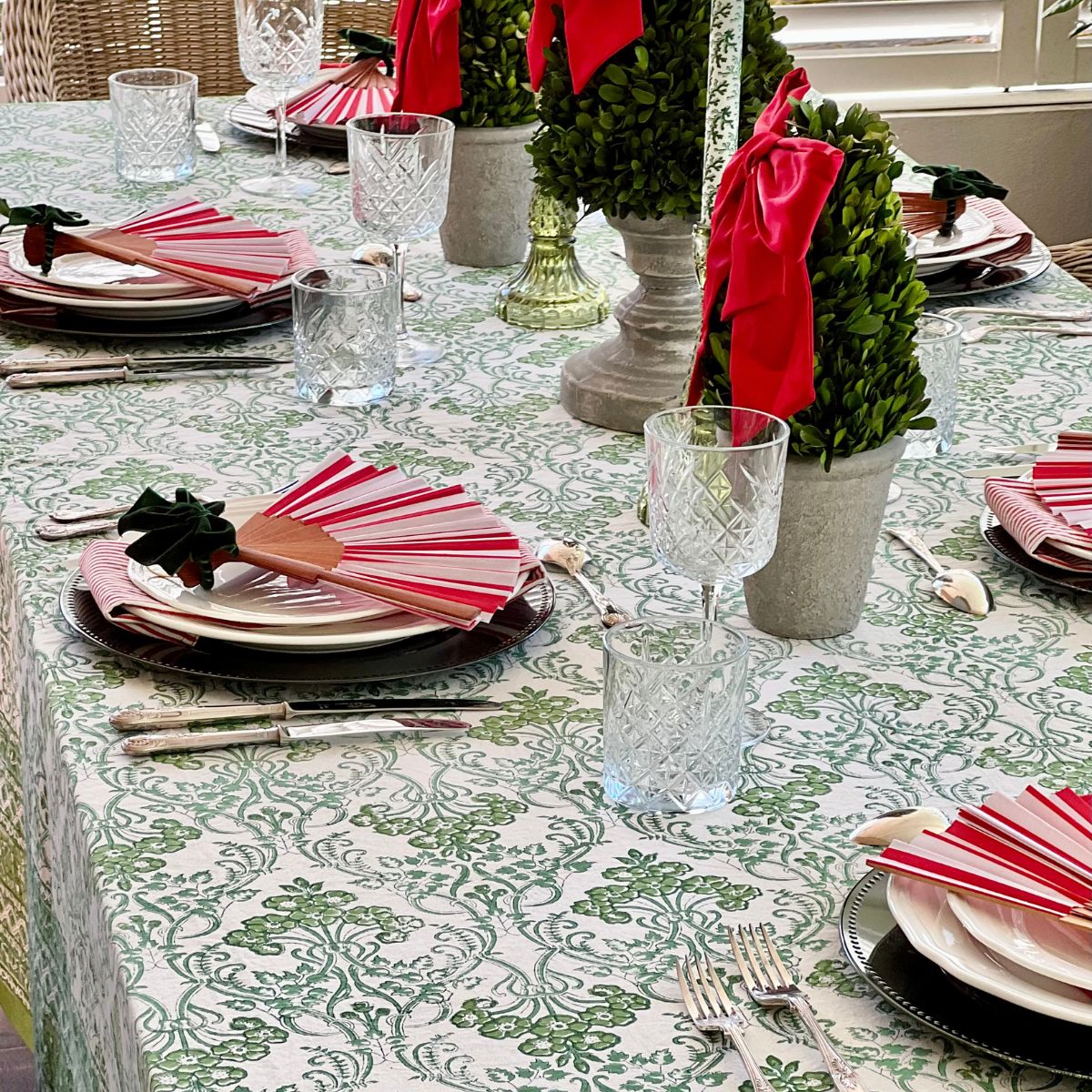Detail of a green floral hand block printed tablecloth in 180 x 270 cm set for Christmas lunch with red white decor. 