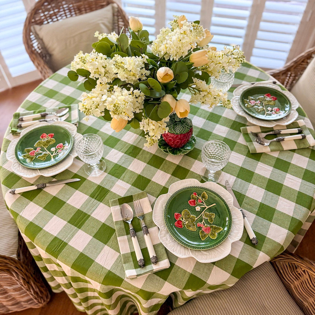Dining table set with green checkered tablecloth, floral centerpiece, and decorative plates.