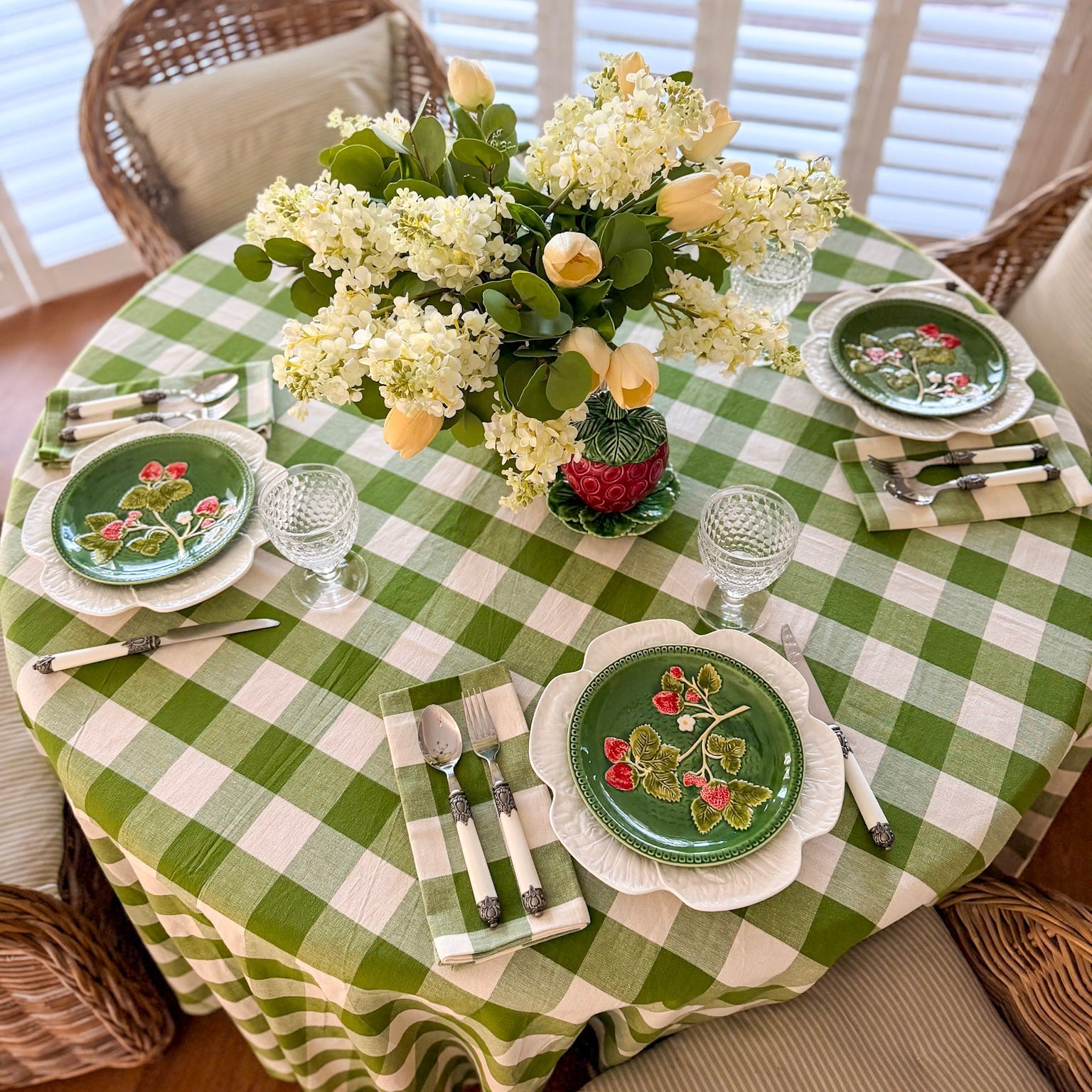 Dining table set with green checkered tablecloth, floral centerpiece, and decorative plates.