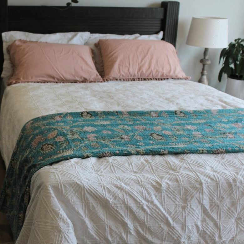 Bed with pink pillows and a floral blanket in a bedroom setting