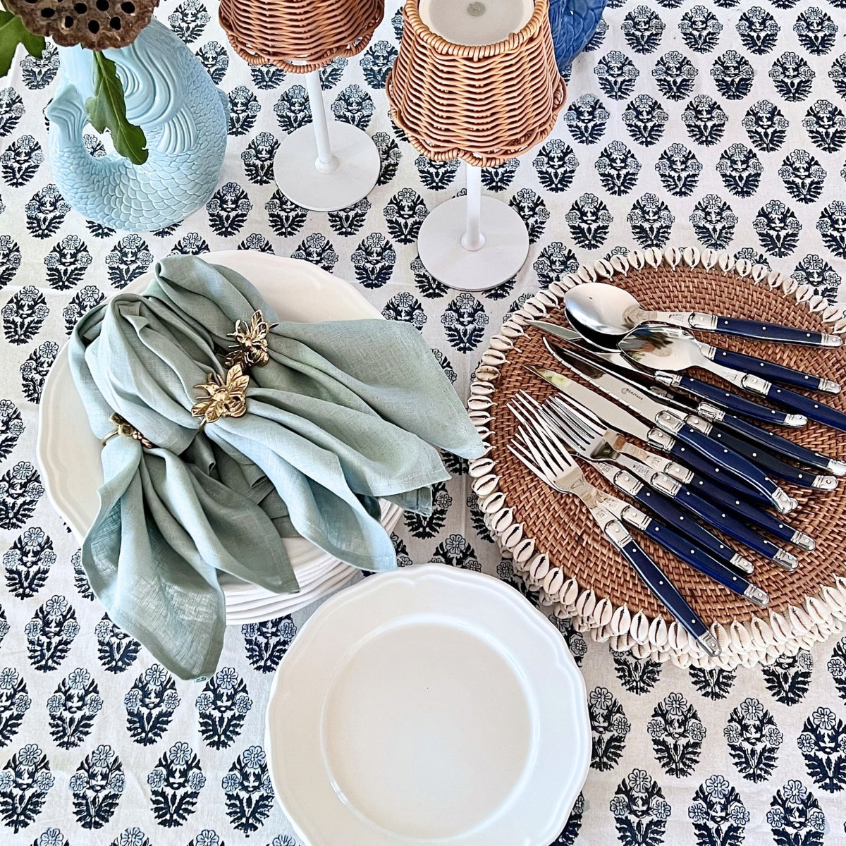 
Blue and white block printed tablecloth styled with sage green napkins, brass napkin rings, rattan placemats and navy handled cutlery