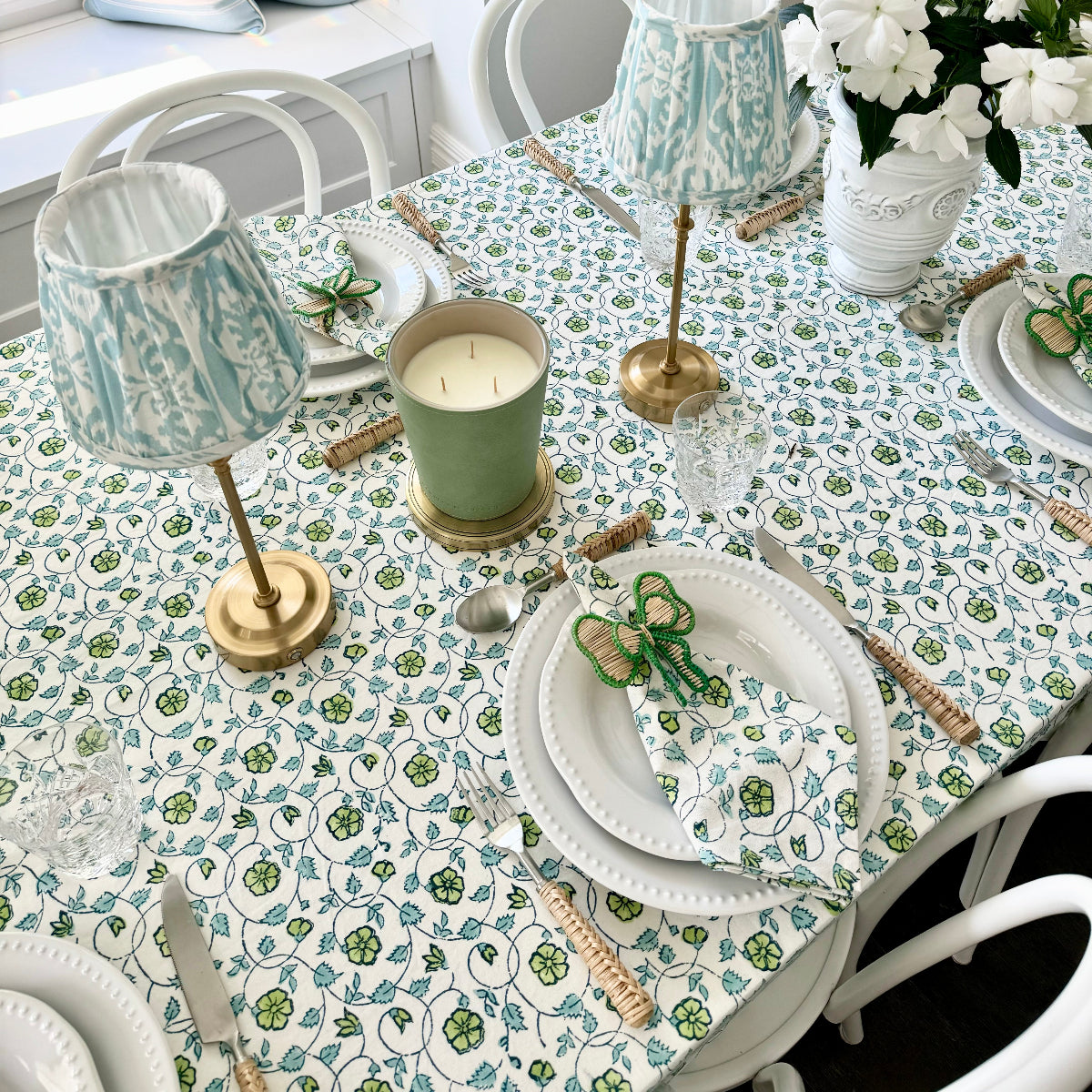 Dining table set with floral tablecloth, green candles, and decorative items.