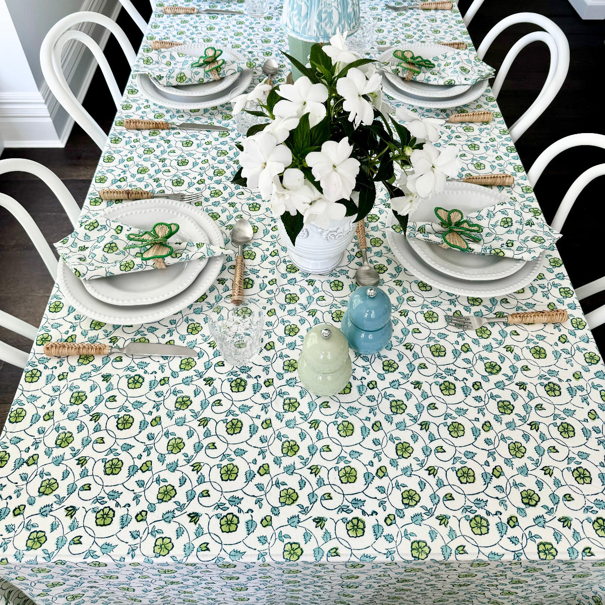 Dining table set with floral tablecloth, green candles, and decorative items.