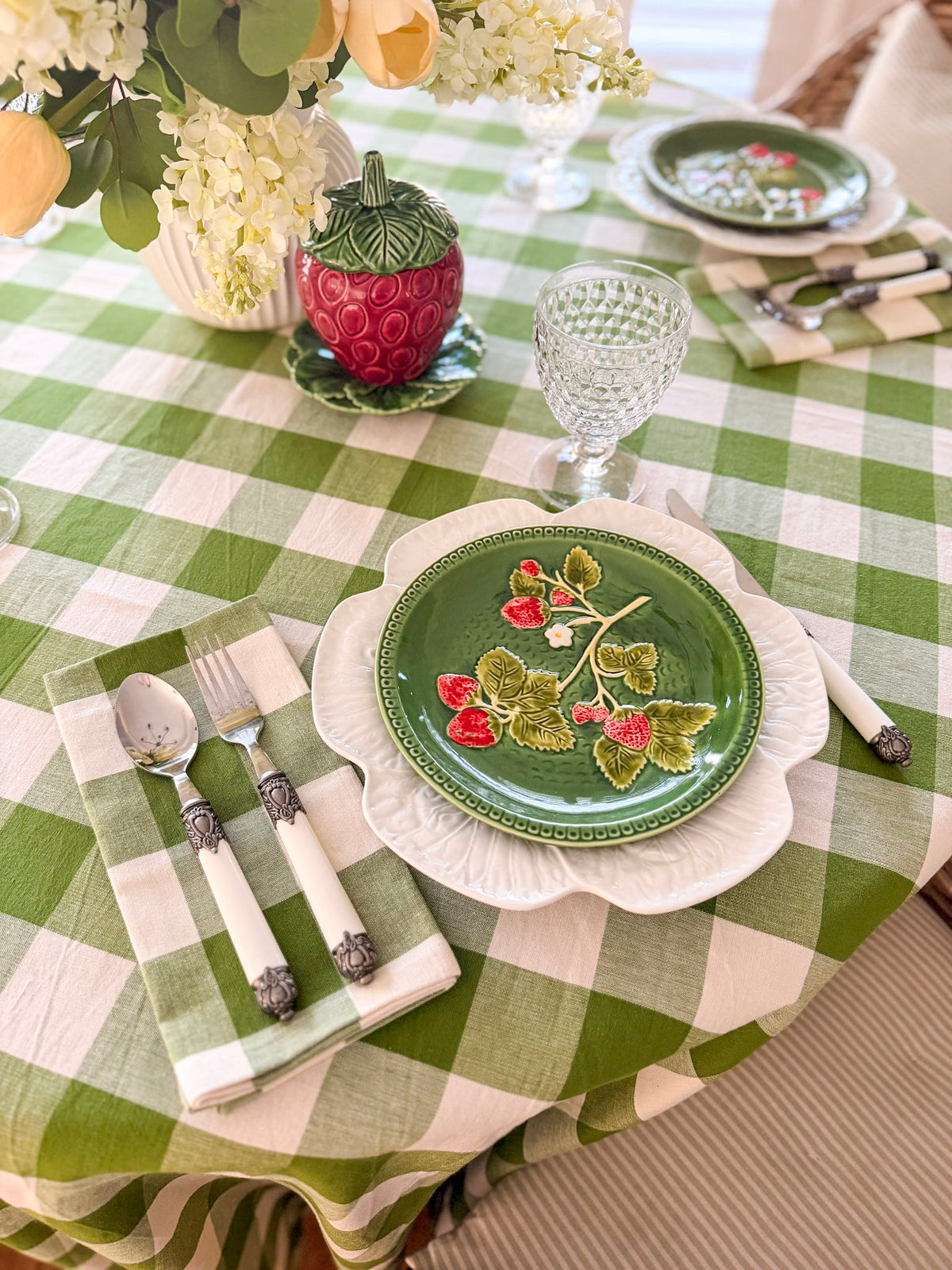Dining table setting with green checkered tablecloth, decorative plates, and floral arrangements.