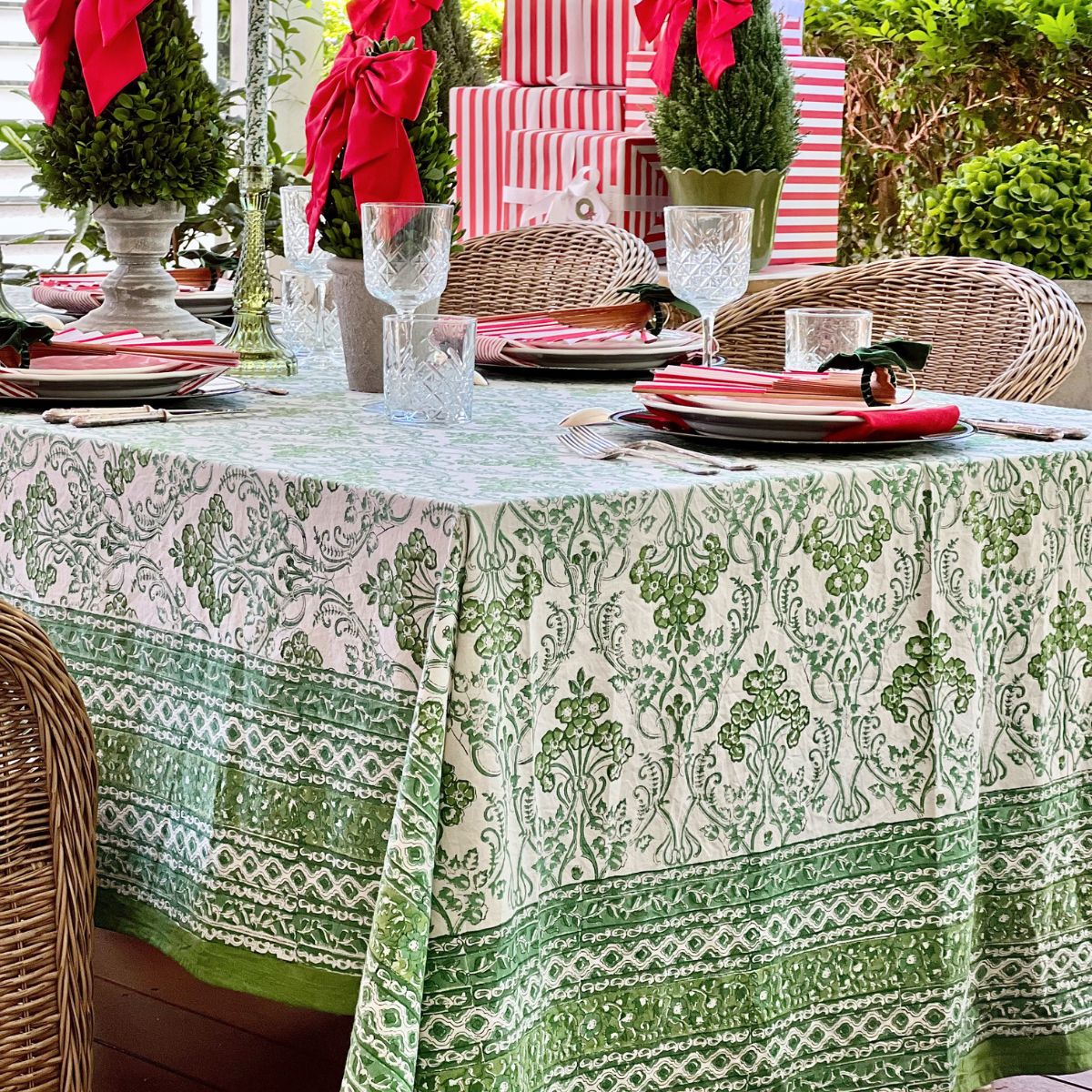 Rectangular green and white hand block printed tablecloth with an intricate border set for a festive Christmas gathering with decorated topiary and festive place settings