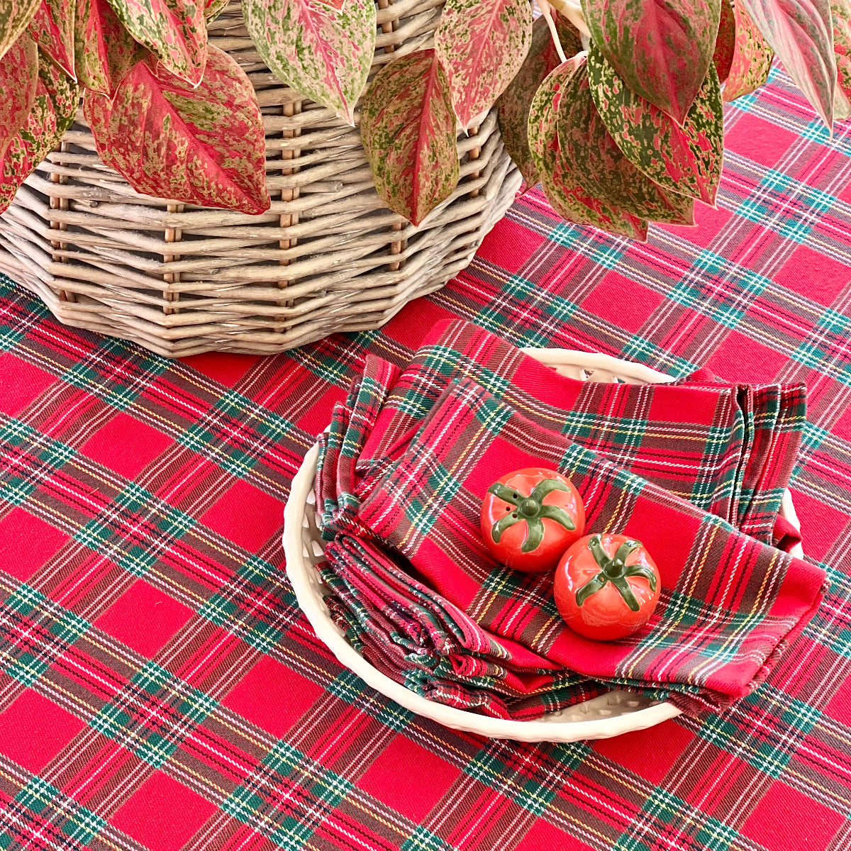 Red plaid tablecloth with a basket, tomatoes, and napkins on a table.