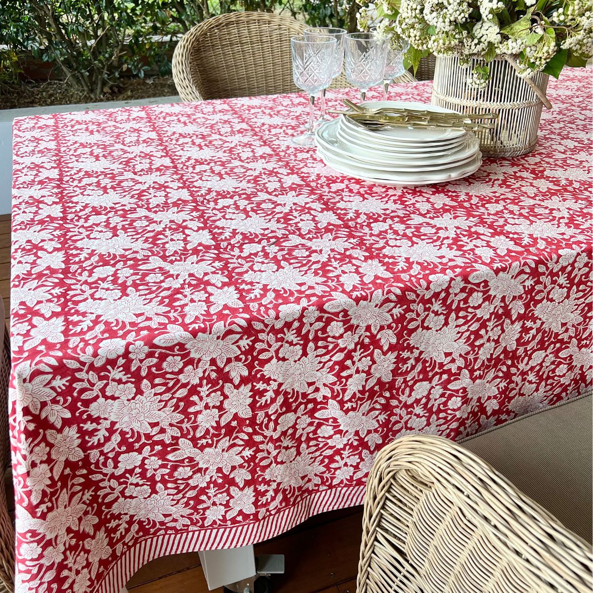 A red and white hand block printed floral patterned tablecloth on a table with plates and cutlery set up for a meal.