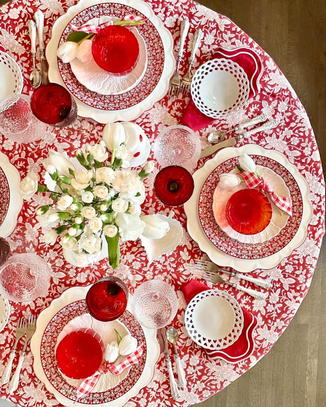 A red and white hand block printed floral patterned round tablecloth on a table, with a vase of flowers and glasses set on top.