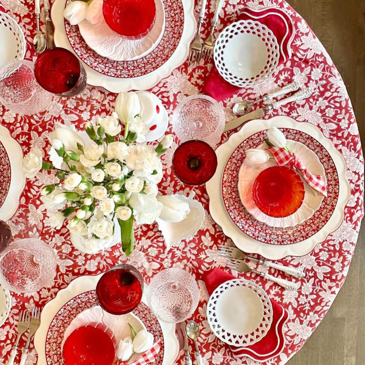 Dining table set with red and white patterned tablecloth, plates, and floral centerpieces.