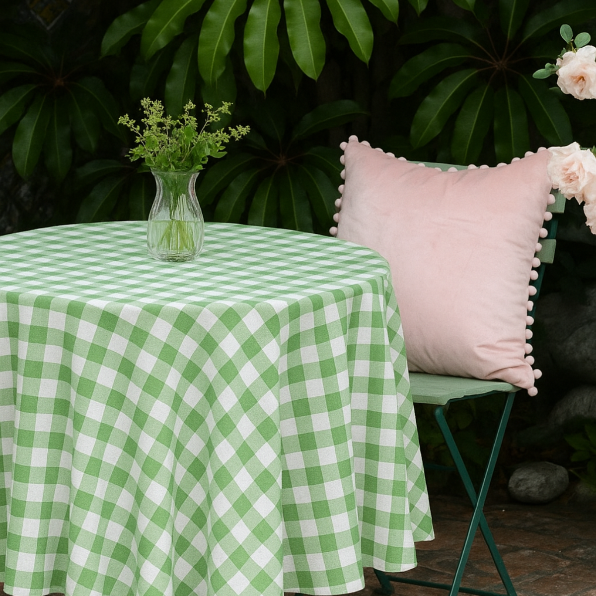 Green and white round gingham table cloth on a round table with a pink cushioned chair and floral decorations.