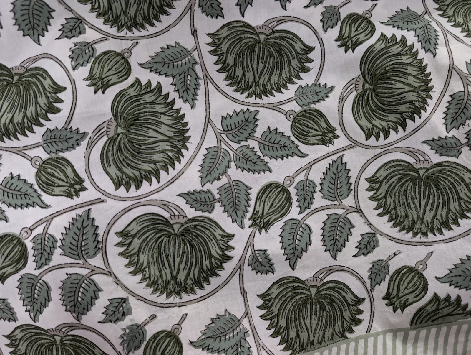 A round tablecloth with a green lotus floral pattern displayed on a table with a white edge.