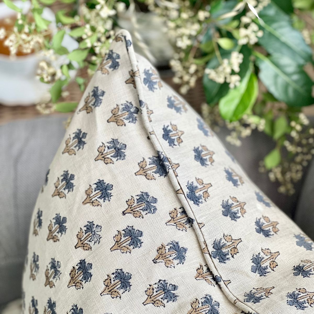
A close-up of the blue palm booti hand block printed pure linen cushion cover on a sofa, showing the edge finish, intricate small floral booti motif and the natural texture of the linen fabric.