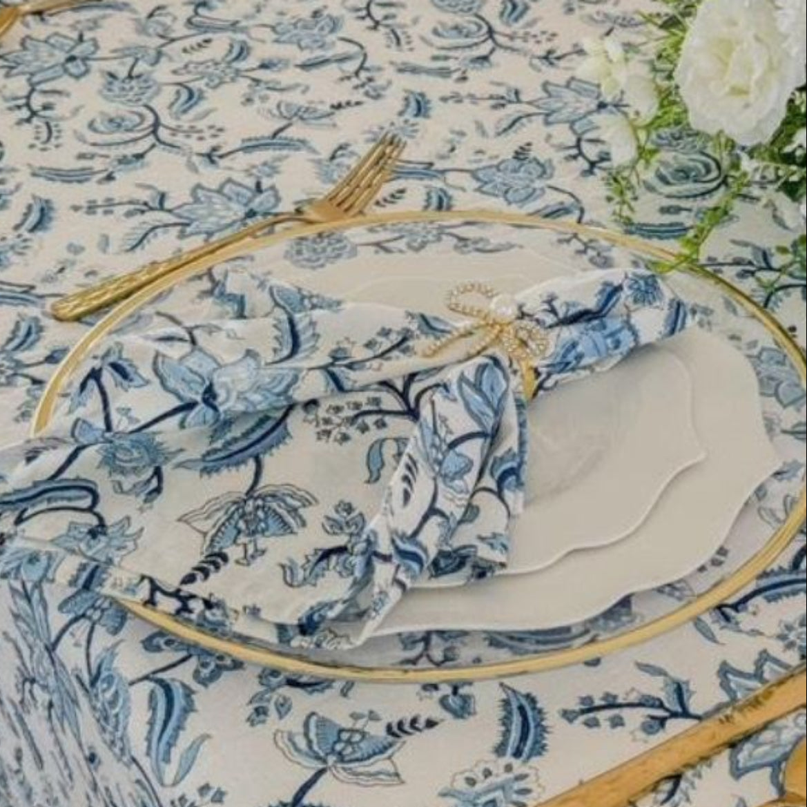A set of four blue and white hand block printed chintz floral patterned napkins on a table with cutlery and a white tablecloth.