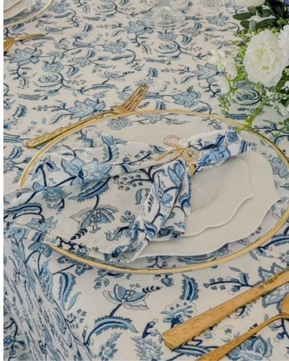 A set of four blue and white hand block printed chintz floral patterned napkins on a table with cutlery and a white tablecloth.